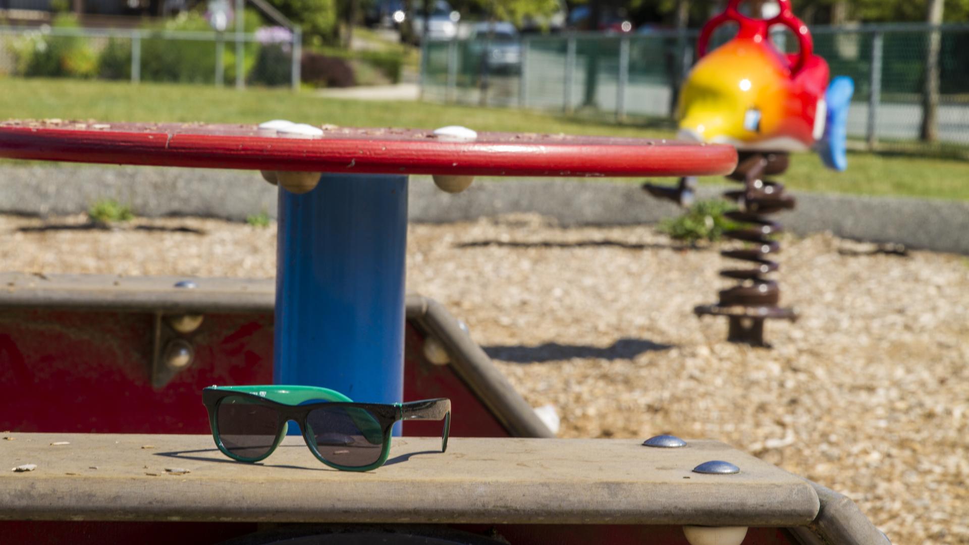 A pair of sunglasses sit on a bench next to a red, circular table. Behind there is a fish shaped spring rider.